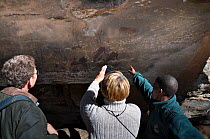 Game reserve guide pointing at cave paintings to visitors with lady taking a photo, Giants Castle, Drakensberg, KwaZulu-Natal, South Africa, July 2009.
