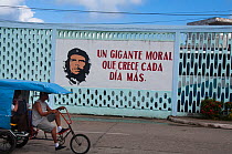 Sign with Che Guevara and a political slogan "Un gigante moral que crece cada dia mas"  which means "A common sense of purpose which grows each day." with a rickshaw passing, Baracoa, Guantanamo provi...