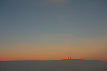 Group of three people silhouetted on sand dune ridge at sunset, White Sands National Park, New Mexico, USA, December 2012.