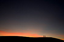 Two people silhouetted on sand dune ridge at sunset, White Sands National Park, New Mexico, USA, December 2012.