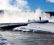 Photographer on wooden walkway with steam rising from geothermal features, Biscuit Basin, Yellowstone National Park, Wyoming, USA, February 2014. MR.
