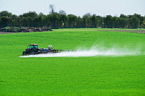 Tractor with a spraying unit spraying cereal crop, showing significant spray drift, Norfol, UK, April.