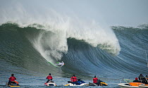 Surfer competing in the Mavericks 2014 surfing competition, watched by people on jet skis, Half Moon Bay, California, USA, January 2014.