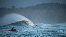 Surfers competing in the Mavericks 2014 surfing competition, with man on jet ski, Half Moon Bay, California, USA, January 2014.