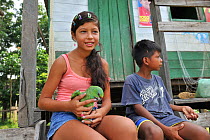 Children of Boca do Mamiraua village with pet  Festive Parrot (Amazona festiva) at Mamiraua Sustainable Development Reserve, Alvaraes, Amazonas State, Northern Brazil, October 2012.