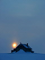 Old house covered in snow with setting sun, Wrangel Island, Far Eastern Russia, March 2011.