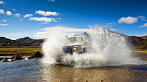 Water spray from 4 by 4 vehicle driving through river, splashing, Iceland.