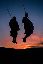 Two Masaai warriors silhouetted performing traditional jump / leap kopje at sunset. Ngorongoro Conservation Area / Serengeti National Park, Tanzania. March 2014.