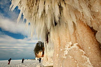 Hikers on frozen lake looking at sea caves and ice formations, Apostle Islands National Lakeshore, Lake Superior, Squaw Bay, Wisconsin, February 2014.