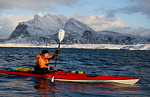 Person paddling a kayak in sea in winter. Donnamannen in background. Heroy municipality, Helgeland, Nordland, Norway. February 2009