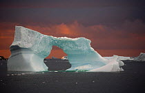 Iceberg with an ice arch grounded in Marguerite Bay at sunset, Antarctica.
