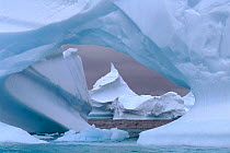 Pointed iceberg seen through a hole in an iceberg near Pleneau Island, Antarctic Peninsula, Antarctica.