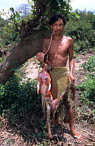 Man with Crab-eating macaque (Macaca fascicularis) caught in trap, dead and skinned, Cambodia.