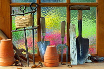 Potting shed window with flower pots,  hand forks, string  and trowel on sill.