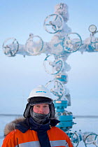 Evgeniy Petrov, a safety officer for Yamal SPG, stands infront of a 'Christmas tree' (valve assembly) at a drilling site in the South Tambey Gas Field, Yamal Peninsula, Siberia, Russia. February 2014.