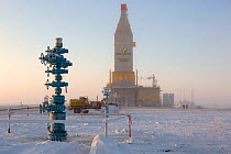 A gas drilling derrick in the distance behind a 'Christmas tree' (valve assembly), South Tambey Gas Field, Yamal Peninsula, Siberia, Russia. February 2014.