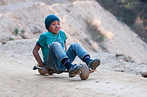 Boy playing with homemade slide toy on wheels. Dirang, Arunachal Pradesh, India. February 2014.