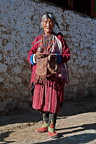 Old lady in traditional Monpa tribe dress (typical head dress made from Yak hair) with prayer mill at the Torgya festival. Galdan Namge Lhatse Monastery, Tawang, Arunachal Pradesh, India. January 2014...
