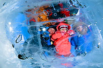 People looking through transparent ice (1m thick) on lake surface to see diver below. Lake Baikal, Russia, March 2012.
