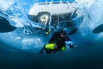 Diver swims under clear transparent ice (1m thick) with vehicle visible above. Lake Baikal, Russia, March 2012.