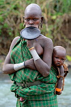 Portrait of Suri / Surma woman wearing lip plate and carrying her baby. Omo river Valley, Ethiopia, September 2014.