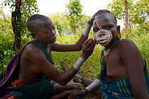 Young Suri / Surma woman painting another woman's face. Omo river Valley, Ethiopia, September 2014.