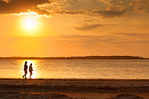 Two people walking along the beach at sunset at the south end of Edisto Island, South Carolina, USA.