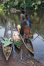 Man and woman with vegetables in dugout wooden canoes on riverbank, Monkoto, Salonga National Park, Equateur, Democratic Republic of the Congo, May 2012.