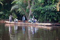 Local people crossing river in wooden dugout canoe, including man with goods on motorbike, Salonga National Park, Equateur, Democratic Republic of the Congo, May 2012.