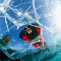 Man looking through transparent ice (1m thick) on lake surface to see diver below. Lake Baikal, Russia, March 2008. Model released.