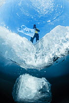 Man visible on surface of the ice through dive hole. Lake Baikal, Russia. March 2008.
