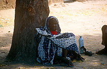 Village elder resting under acacia tree with  bottle of milk, rural Chad, 2002-2003.