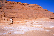 Local man sat by ancient rock engravings of human and animal figures, thought to be at least 8000 years old. Northern Niger, 2005.