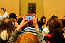 Tourists crowding round the Mona Lisa by Leonardo DaVinchi and taking photographs on cameras and phones,  the Louvre, Paris, France, November 2013.