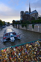 Padlocks on the Pont de l'Archeveche bridge and Notre Dame Cathedral, with boat passing, Paris, France, October 2013.