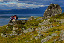 Teenage girls sitting on rocks overlooking the sea, on family hiking trip on the Laponia Circuit. Padjelantaleden trail, Padjelanta National Park and Sarek National Park, Norrbotten, Lapland, Sweden....