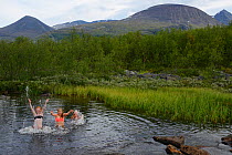 Woman and two teenage girls splashing in river on hiking trip, Laponia Circuit, along the Padjelantaleden trail, Padjelanta National Park and Sarek National Park, Norrbotten, Lapland, Sweden. Model re...