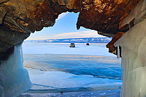 View through rock arch of vehicles parked on ice on the surface of Lake Baikal, Siberia, Russia, March 2012.