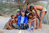 Photographer Eric Baccega showing pictures to Naro San Bushmen family with children wearing traditional clothing made with duiker leather. Kalahari, Ghanzi region, Botswana, Africa. Dry season, Octobe...