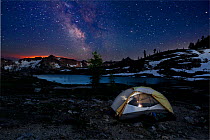 Campsite at night in Snowy Lakes Basin, glow of forest fire on the horizon. North Cascades area of the Okanogan Wenatchee National Forest, Washington, USA, July 2014. Model released.