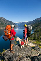 Backpackers with dog looking out over lake on the Lake Chelan Trail between Moore Point and Stehekin, Lake Chelan-Sawtooth Wilderness, Washington, USA, May 2014. Model released.