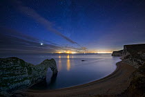 Stars and Milky Way over Durdle Door and the Jurassic Coast, with the lights of Weymouth and Portland beyond, Dorset, England, UK, December 2013.