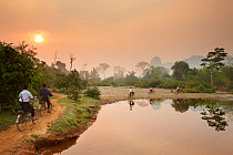 Children riding bikes along riverside path at dawn, near Vang Vieng, Laos, March 2009.