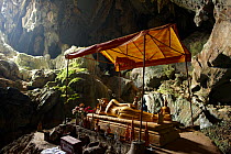 Statue of the reclining Buddha with smaller statues around in a cave, the Blue Lagoon, near Vang Vieng, Laos, March 2009.
