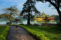 Woman walking along path with parasol, with Karaweik Palace in the background, Kandawgyi Lake, Yangon, Myanmar, November 2012.