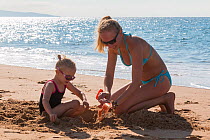 Mother and daughter playing with a spade on the beach. Biarritz, Aquitaine, France, September 2014. Model released.