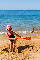 Young girl with plastic spade digging hole on the beach. Biarritz, Aquitaine, France, September 2014. Model released.