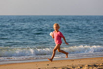 Young girl running along beach with soft toy. Biarritz, Aquitaine, France, September 2014. Model released.