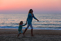 Mother and daughter playing, running along beach at sunset. Biarritz, Aquitaine, France, September 2014. Model released.