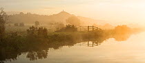 River Brue on a misty dawn with Glastonbury Tor in background, Somerset, UK, October, digital composite.